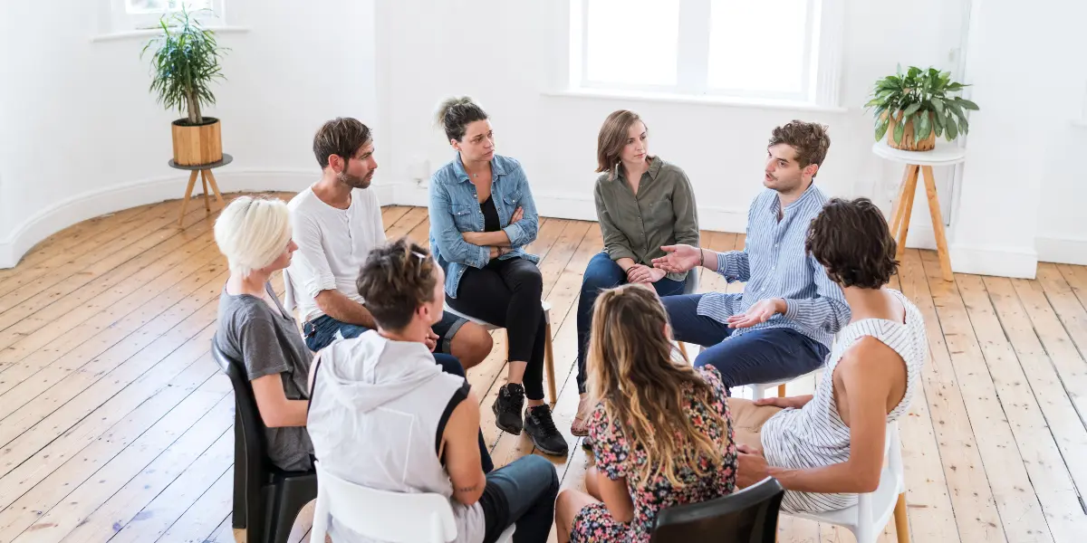 Grupo de personas adultas conversa en círculo durante una sesión grupal.