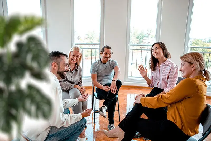 Cinco personas adultas conversan sentadas en círculo en una sala luminosa.